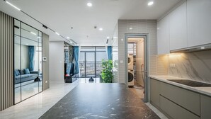 A modern kitchen with a marble countertop, built-in cabinets, and a view to the living area. - Wow! Homes by Christine - Vinhomes Luxury (Ho Chi Minh City)