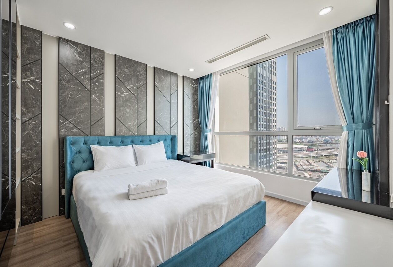 A modern hotel room with a large bed, a view of the city through a large window, and a balcony with a view of the cityscape.