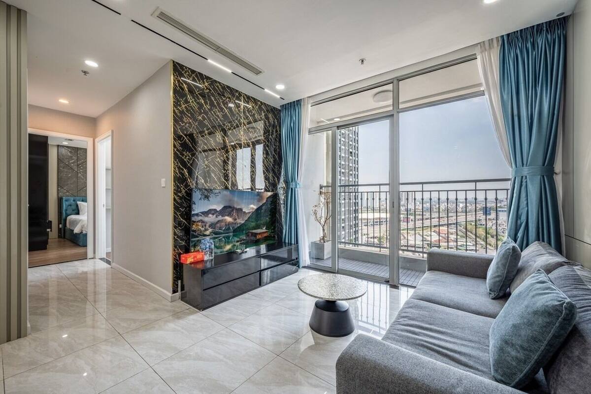 Ein modernes Wohnzimmer mit großem Fernseher, einer Couch und einem Balkon mit Blick auf die Stadt.