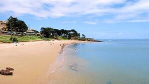 Une plage à l’eau claire, avec un rivage sablonneux et une zone herbeuse parsemée d’arbres.