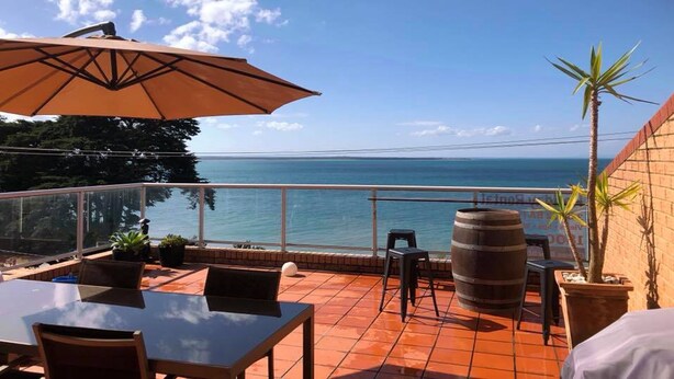 Une terrasse avec vue sur la mer, comprenant une table, des chaises, un parasol et un tonneau.