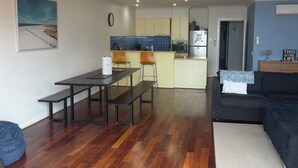 Un vaste espace de vie doté d’un plancher en bois, d’une table à manger avec des bancs, d’un canapé et d’une cuisine à l’arrière-plan.