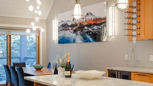 A modern kitchen with a large island, bar stools, pendant lighting, and a scenic painting on the wall.