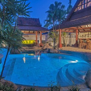 A swimming pool with a clear blue water feature, surrounded by tropical plants and a covered seating area with a red roof. - Samui Little Garden Resort (Koh Samui)