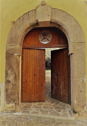 Uma porta arqueada com portas de madeira, dando acesso a um caminho de pedras.