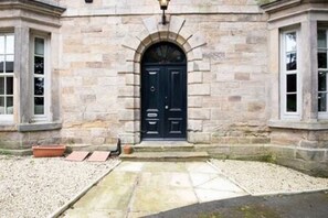 Un edificio de piedra con una puerta negra, un pequeño porche y un camino de grava que lleva a la entrada.