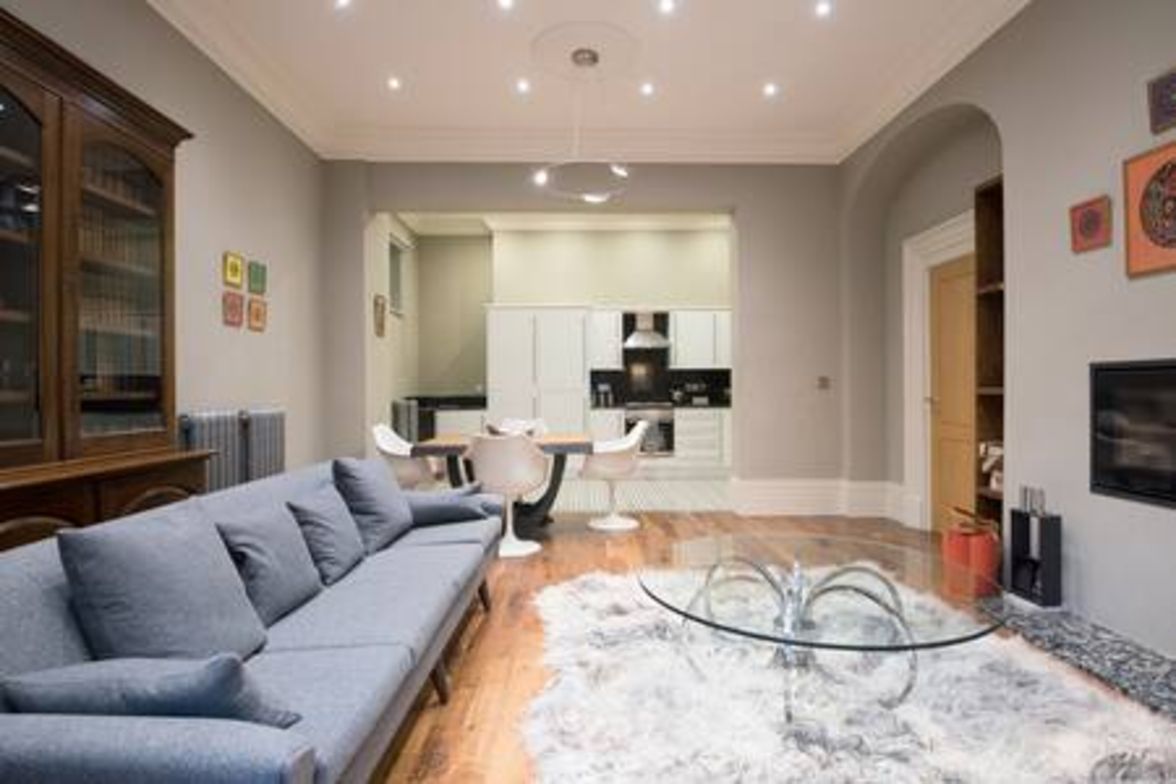 A modern living room with a sofa, a glass coffee table, and a kitchen in the background.