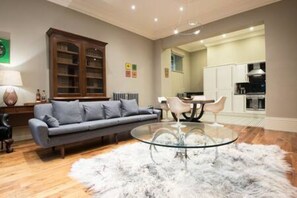 Una sala de estar moderna con un sofá gris, una mesa de centro de vidrio y una alfombra blanca y mullida.