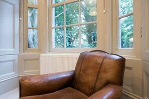 Una habitación con un sillón de cuero marrón, una ventana de varios paneles y paredes con paneles blancos.