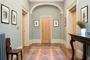 Un pasillo con un tapete estampado, cuadros en las paredes y una puerta de madera al final.