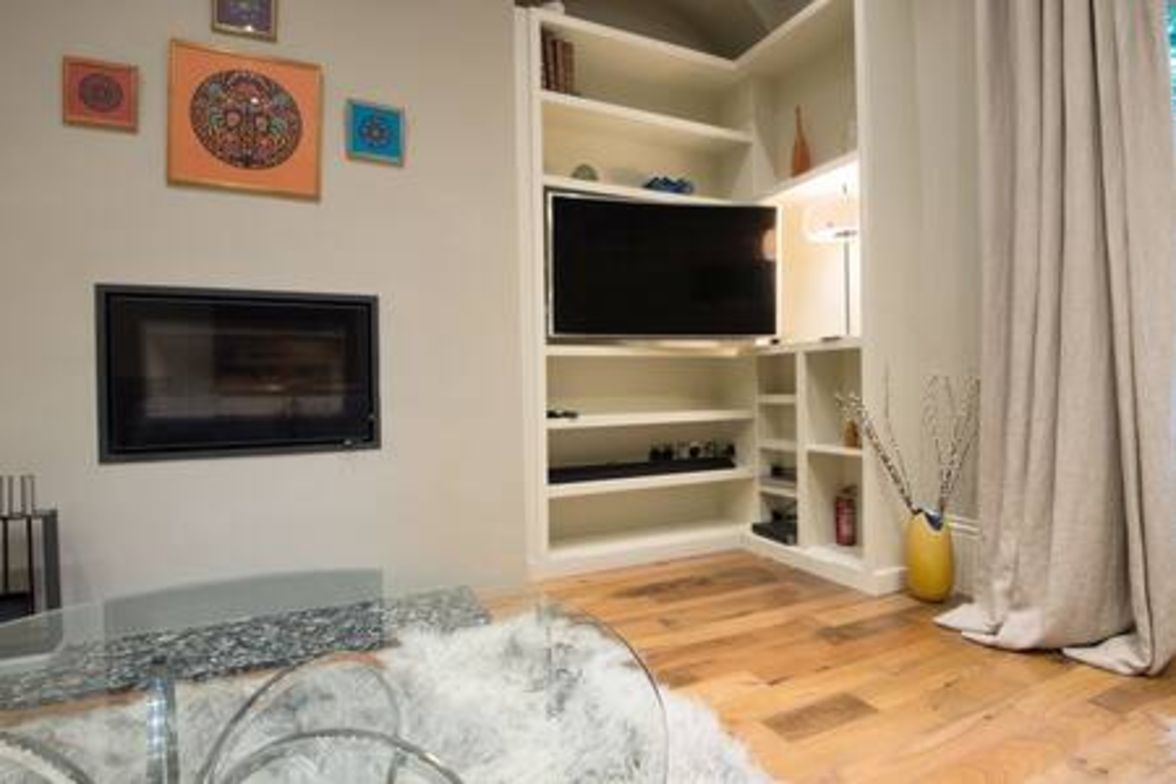 A living room with a flat-screen TV, shelves, and a glass coffee table.