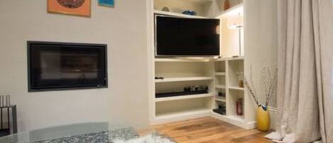 A living room with a flat-screen TV, shelves, and a glass coffee table.