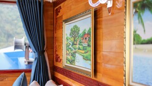 A room with wooden paneling, a framed painting of a landscape, a window with curtains, and a view of the outdoors. - La Paci Cruises (Hai Phong)