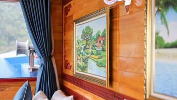 A room with wooden paneling, a framed painting of a landscape, a window with curtains, and a view of the outdoors.