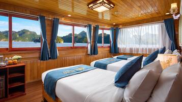 A cabin with two beds, wooden walls, and large windows offering a view of the water and hills.