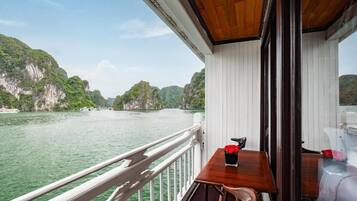 A balcony with a wooden table and chairs, overlooking a river with cliffs.