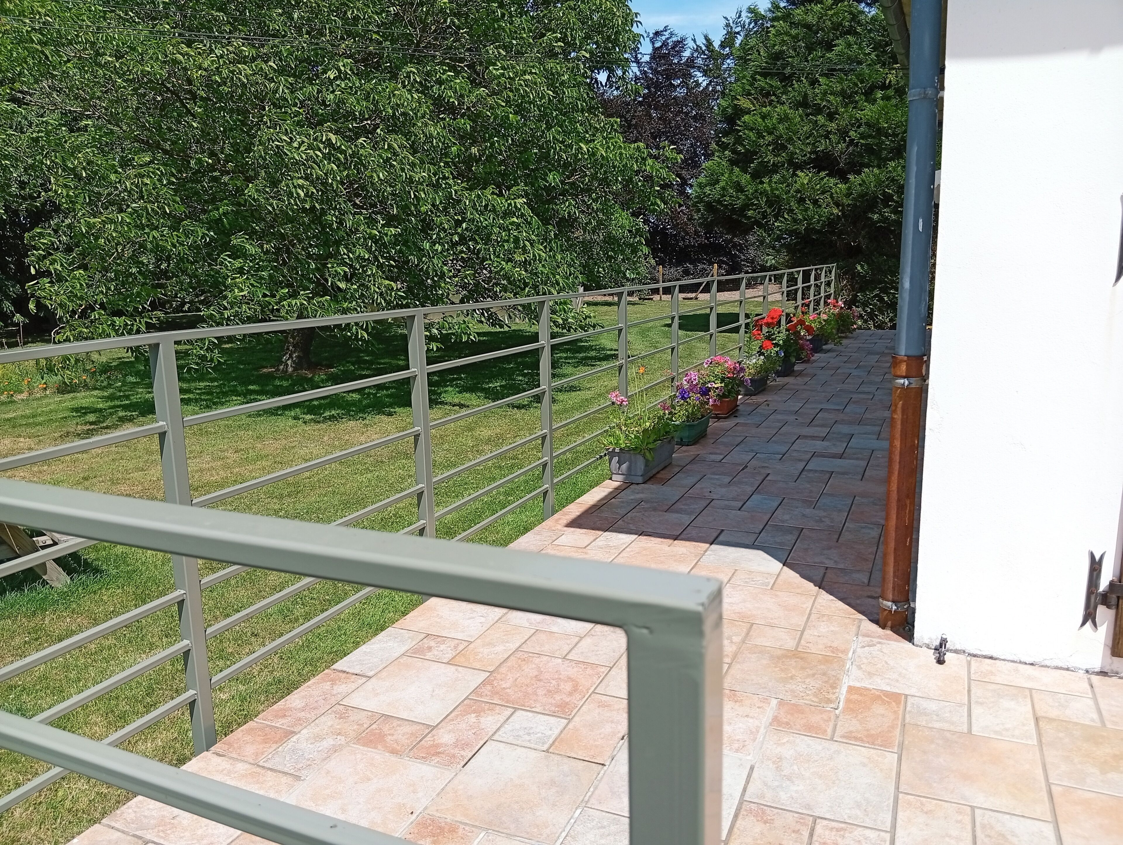 Un balcon doté d’une rambarde en métal, de plantes en pot et d’un sol carrelé.
