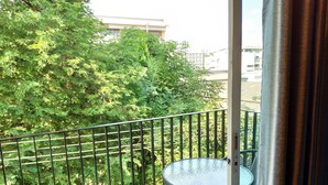A balcony with a table and chairs, surrounded by a metal railing, overlooking a lush green area with trees and buildings in the background. - Ninety 9 Hostel (Bangkok)