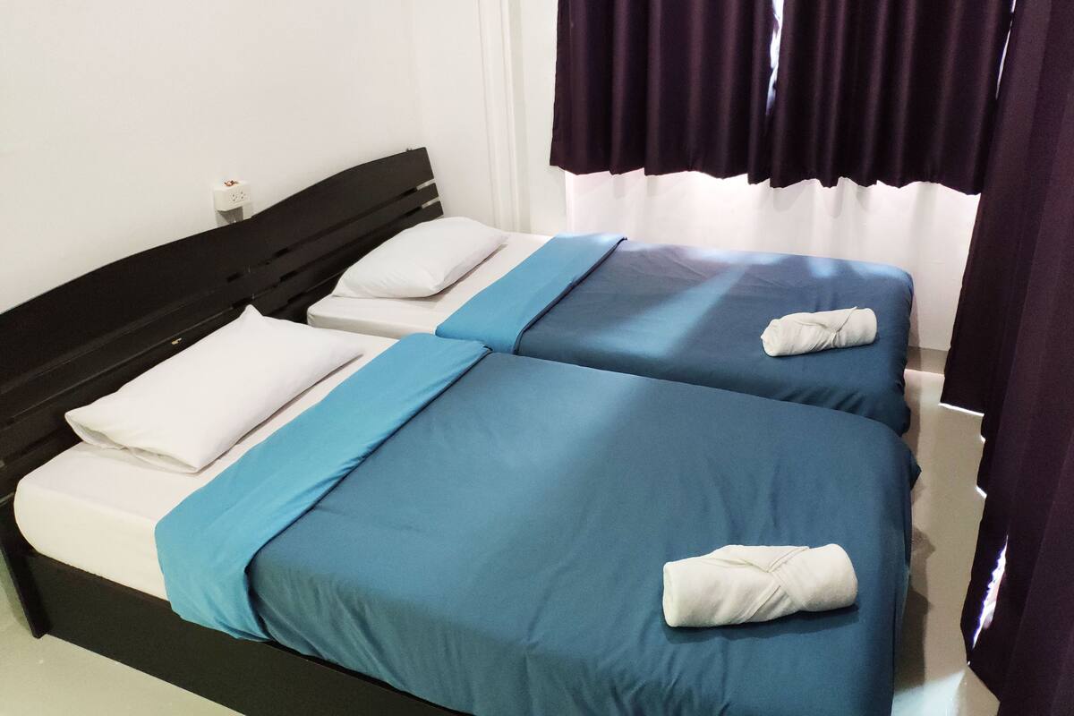 A hotel room with two single beds, each with a blue bedspread and white pillows.