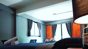 A hotel room with two beds, a desk, and a chair. There are curtains on the windows, and a lamp is on the desk. - Ninety 9 Hostel (Bangkok)