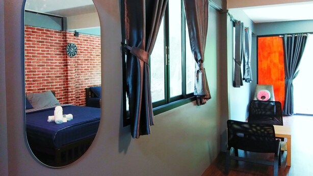 A room with a bed, a round mirror, a window with curtains, a clock on the wall, and a small table with a chair. - Ninety 9 Hostel (Bangkok)
