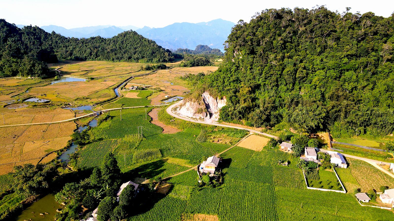 An aerial view of a rural landscape with terraced fields, a river, and a forested hill.
