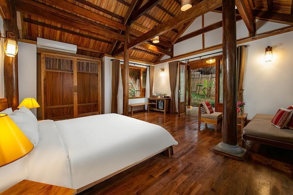 Une pièce spacieuse avec un grand lit, un plancher en bois et un plafond haut avec des poutres apparentes. On y trouve un bureau avec une chaise et une petite table avec un banc.