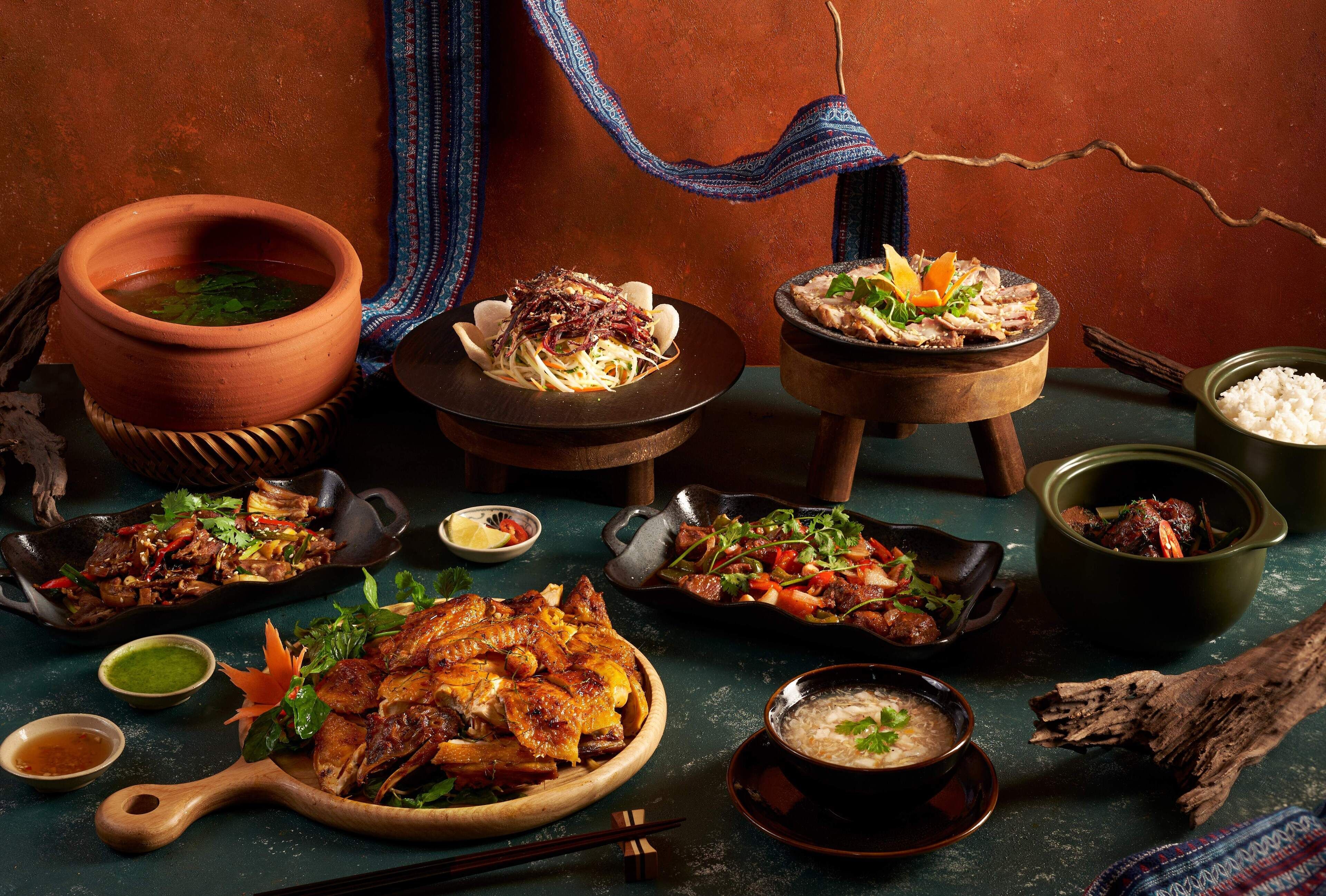 A variety of dishes including a large roasted chicken, a bowl of soup, and several side dishes on a table with a rustic setting.