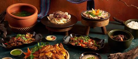 A variety of dishes including a large roasted chicken, a bowl of soup, and several side dishes on a table with a rustic setting.