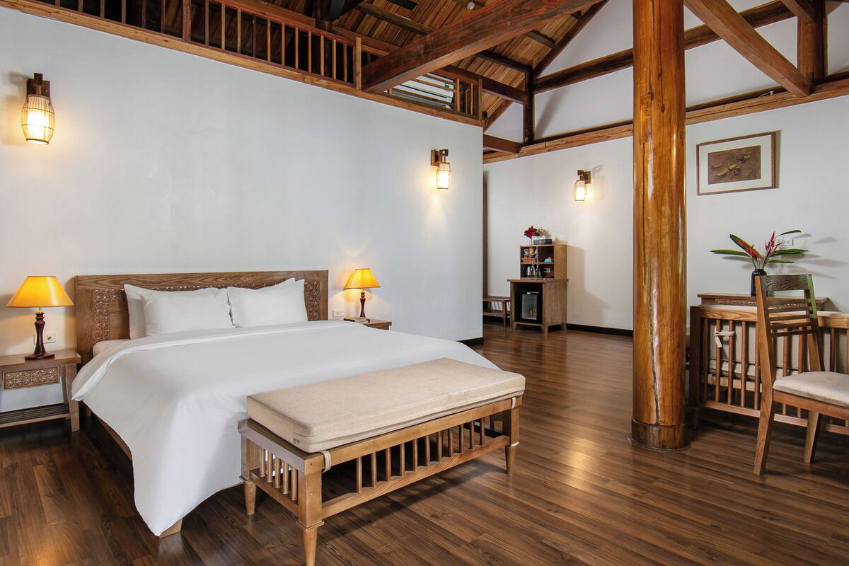 Une chambre spacieuse avec un grand lit, un plancher en bois et un ventilateur de plafond.