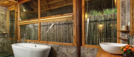 A bathroom with a freestanding bathtub, a wooden vanity, and a large window with a bamboo screen.