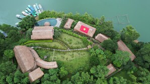 Luchtbeeld van een resort met een zwembad, bungalows met rieten daken en een vlag.