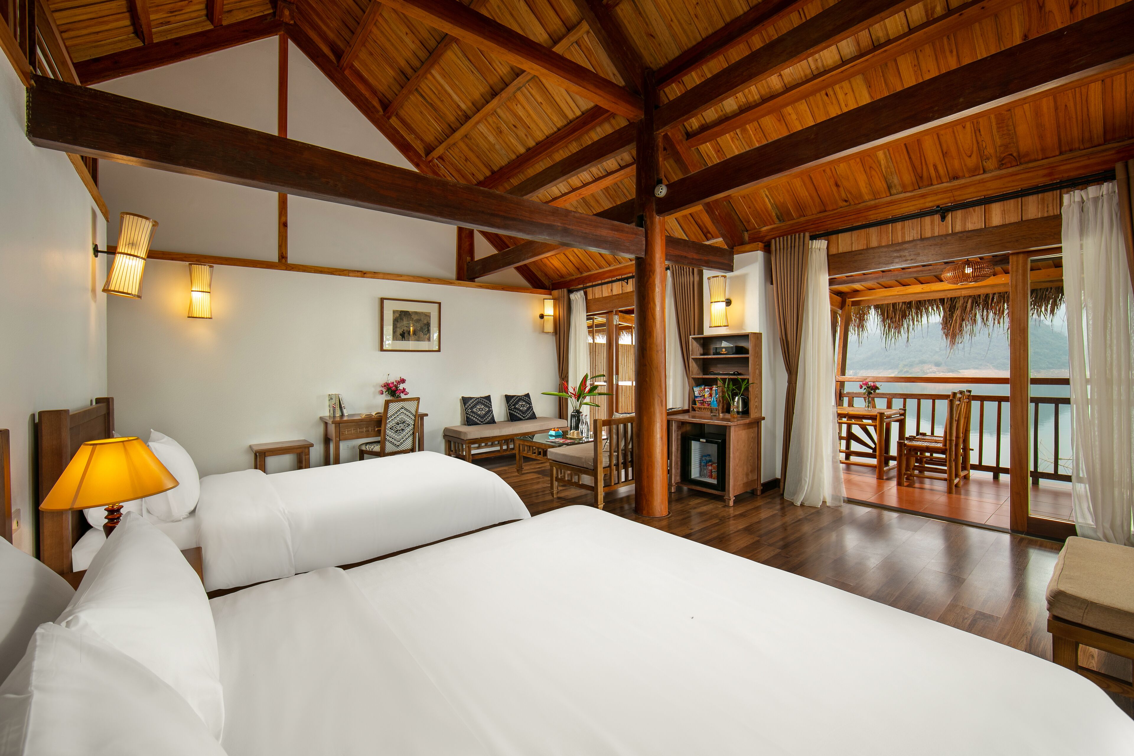 A spacious room with a large bed, wooden ceiling beams, a dining area, and a view of the sea.