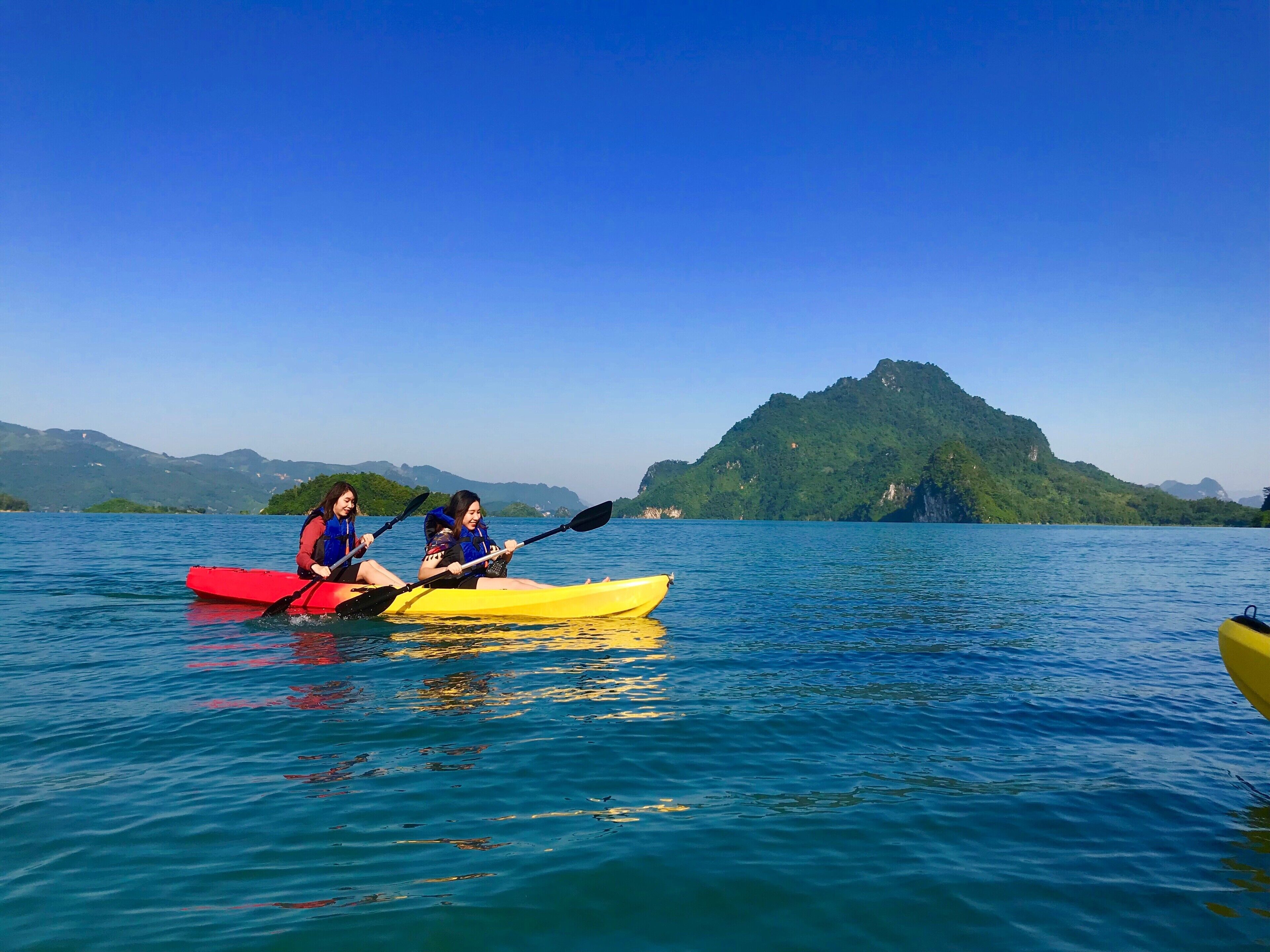 Two people kayaking on a calm lake with a mountain in the background.