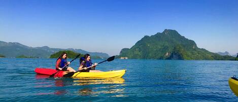 Two people kayaking on a calm lake with a mountain in the background.