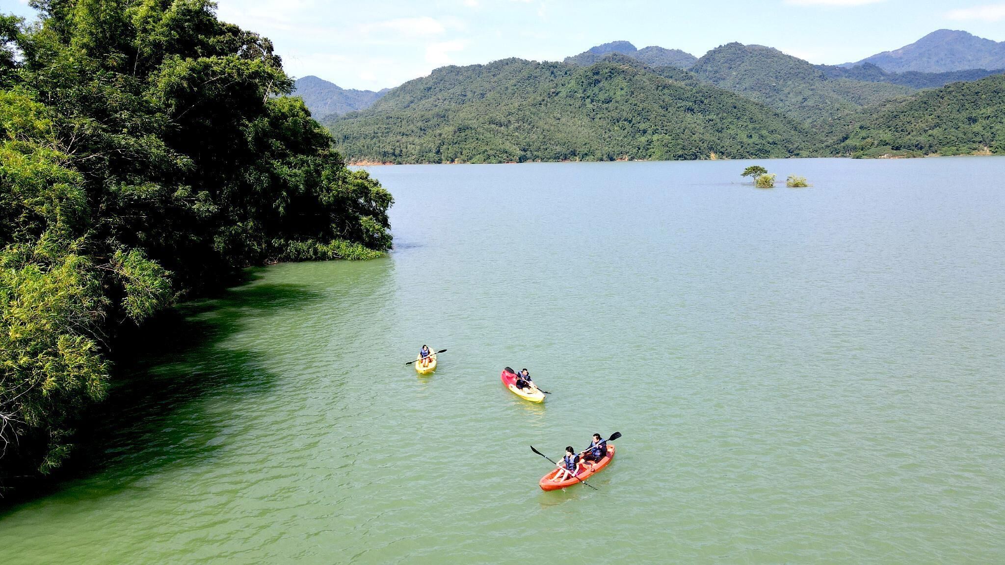 A calm lake with kayaks on the water and dense forest on the shore.