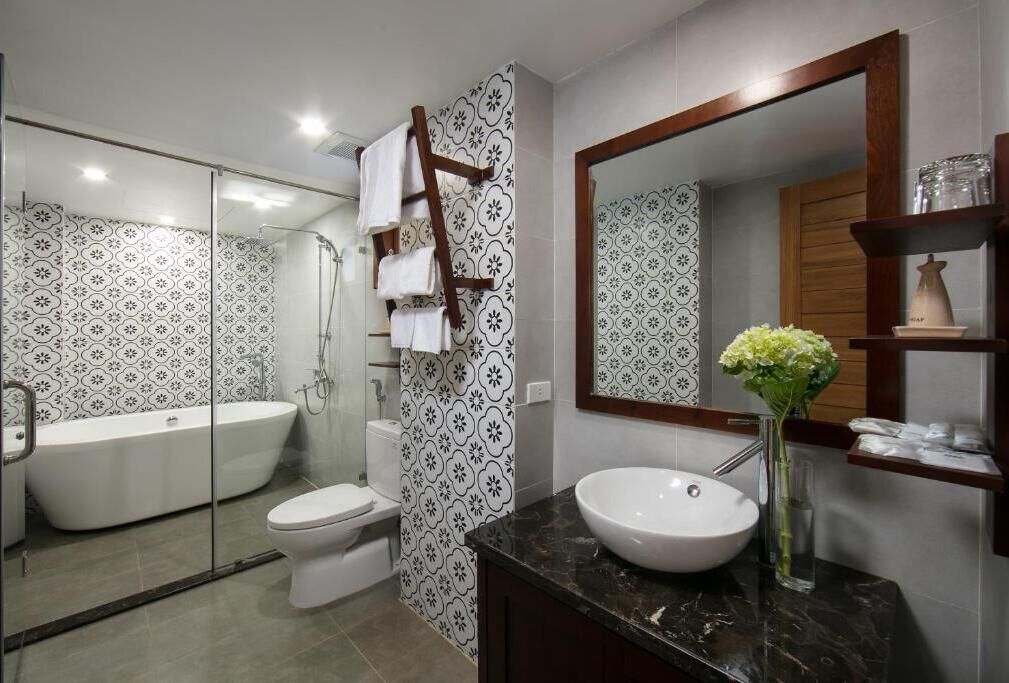 Un baño moderno con cabina de ducha de vidrio, una bañera blanca, inodoro y tocador con un espejo grande y un florero.