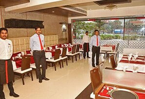 A restaurant with tables set for dining, a bar area, and a view of the outdoors. - Hotel South Coast (Navi Mumbai)