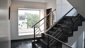 A modern staircase with a metal railing, leading to a landing with a large window offering a view of greenery outside. - Hotel South Coast (Navi Mumbai)