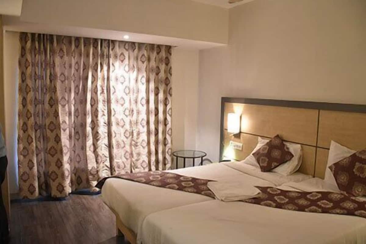 A hotel room with two beds, a nightstand, a lamp, and a window with patterned curtains.