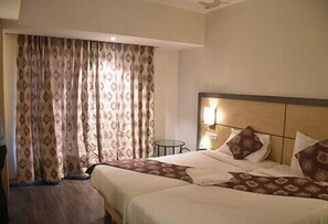 A hotel room with two beds, a nightstand, a lamp, and a window with patterned curtains. - Hotel South Coast (Navi Mumbai)