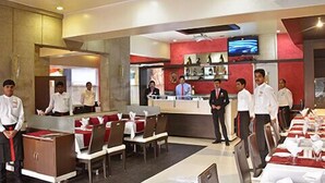 A restaurant with multiple tables set for dining, a counter with staff, and a television on the wall. - Hotel South Coast (Navi Mumbai)