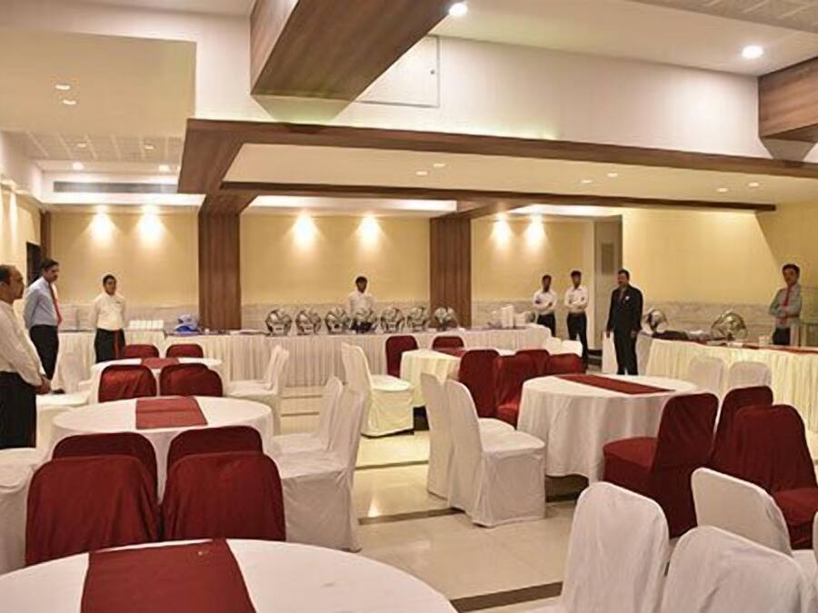 A banquet hall with round tables covered in white tablecloths and red chair covers, arranged in rows.