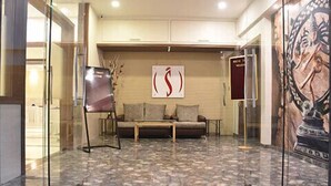 A lobby with a sofa, a glass wall, and a poster on the wall. - Hotel South Coast (Navi Mumbai)