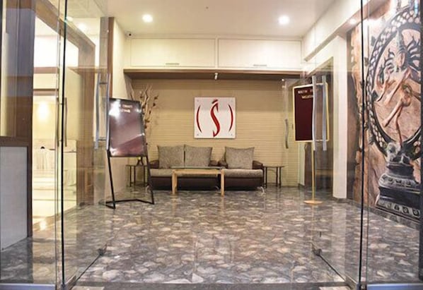 A lobby with a sofa, a glass wall, and a poster on the wall. - Hotel South Coast (Navi Mumbai)