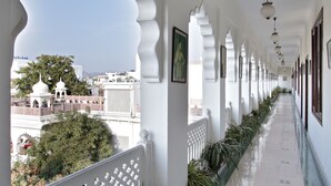 A corridor with white walls, patterned floor tiles, and a row of potted plants. - Khandwa Haveli (Jaipur)