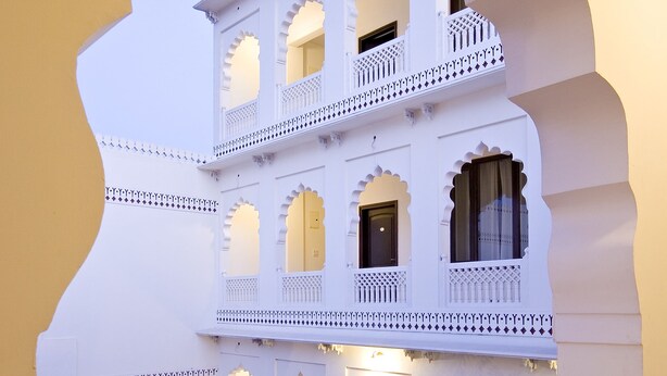 A multi-story building with ornate balconies and arched windows, featuring a courtyard with potted plants and a seating area. - Khandwa Haveli (Jaipur)