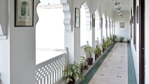 A corridor with white walls, decorative arches, potted plants, and framed pictures. - Khandwa Haveli (Jaipur)