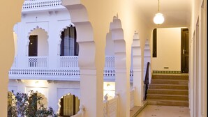 A corridor with white arches, a staircase, and a hanging light fixture. - Khandwa Haveli (Jaipur)