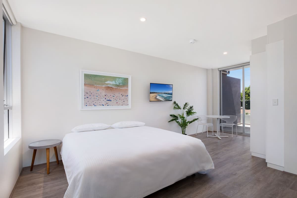 Un dormitorio moderno con una cama grande, una mesita auxiliar pequeña, una planta en maceta y vistas al exterior a través de un ventanal corredero.